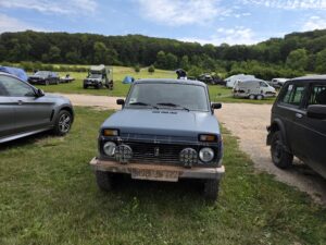Blaugrauer Lada Niva mit Zusatzscheinwerfern, dahinter der Zeltplatz des Niva-Treffens