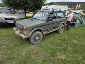Grüner Lada Niva Taiga 4×4 auf der Wiese neben einem Wohnwagen