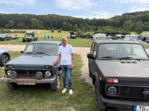 Teilnehmer im hellen Poloshirt zwischen zwei Lada Niva auf dem Campingplatz
